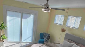 Un dormitorio con una cama grande, un ventilador de techo, una planta en maceta y una silla.