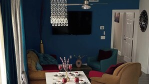 Un comedor con una mesa preparada para cuatro personas, un sofá y un televisor montado en la pared.