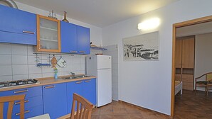 Una cocina compacta con armarios azules, un refrigerador blanco y una silla de madera.