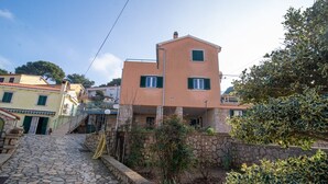 Una calle empedrada que lleva a un edificio de dos pisos con fachada de piedra y contraventanas verdes.