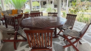 Eine überdachte Terrasse im Freien mit einem Reetdach, Holzmöbeln und einem Steinboden.