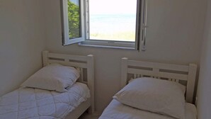 Two single beds with white bedding in a room with a window overlooking a beach. - Lacic / Lacic B4 in Mali Lošinj (Mali Lošinj)