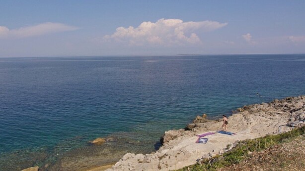 A coastal scene with clear blue water, rocky shoreline, and a person walking on the beach. - Lacic / Lacic B4 in Mali Lošinj (Mali Lošinj)