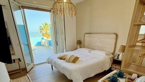 A bedroom with a bed, bedside table, and a view of the sea.
