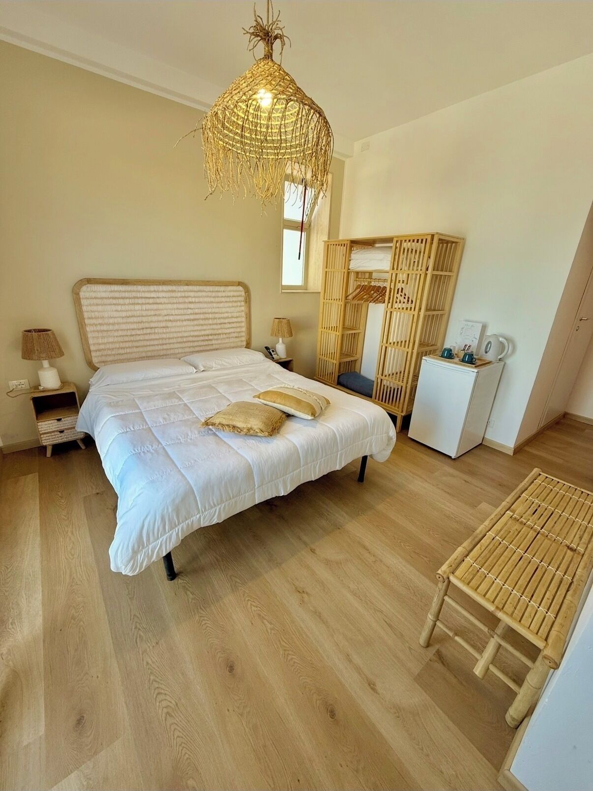 A bedroom with a bed, bedside lamps, a wardrobe, a small fridge, and a hanging light fixture.