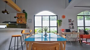 A modern kitchen with a large window, wooden chairs, a blue table, and a bar area with stools. - Converted Chapel Villa · Private Pool + Arcade (Dumaguete City)