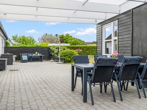 Un patio con mesa y sillas, un rincón de descanso con sofá y mesa, y una valla de madera.