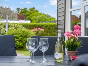 A table with two empty wine glasses, a bottle of white wine, and a potted plant with pink flowers. - "Elene" -  from the sea by Interhome (Hadsund)