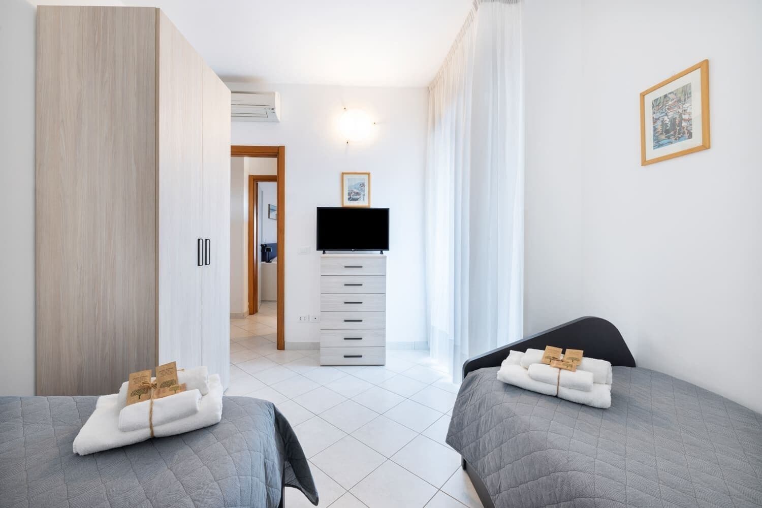 A hotel room with two beds, a wardrobe, a television, and a framed picture on the wall.