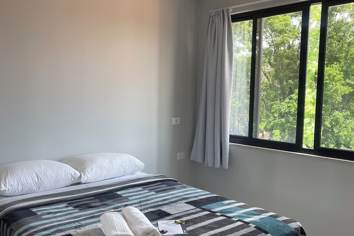 A bedroom with a bed, pillows, a striped blanket, and a window with curtains.