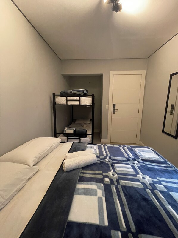 A bedroom with a bunk bed, a single bed, a patterned bedspread, and a door. - Social Hostel (Curitiba)