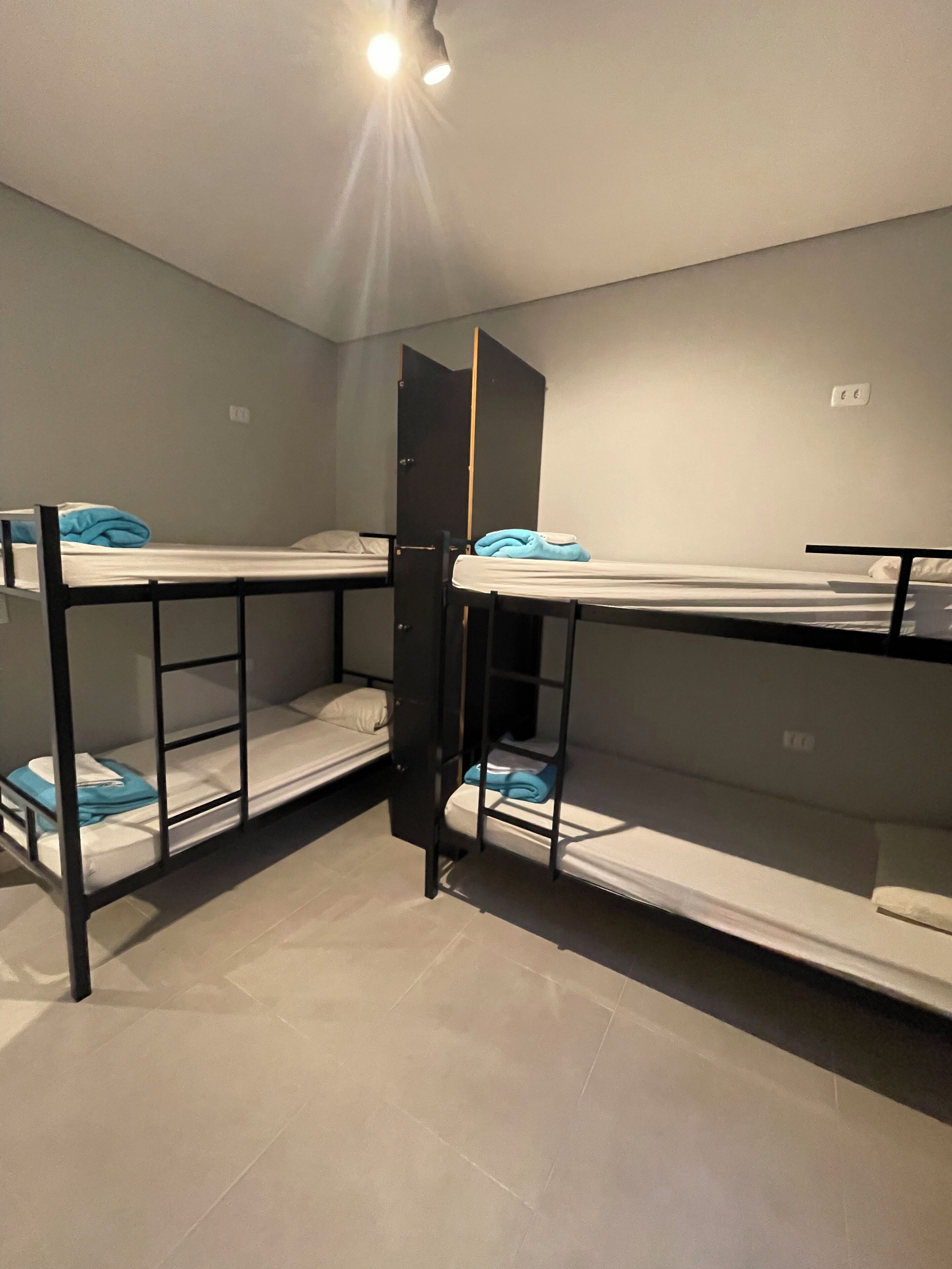 A dormitory room with bunk beds, a wardrobe, and a ceiling light.