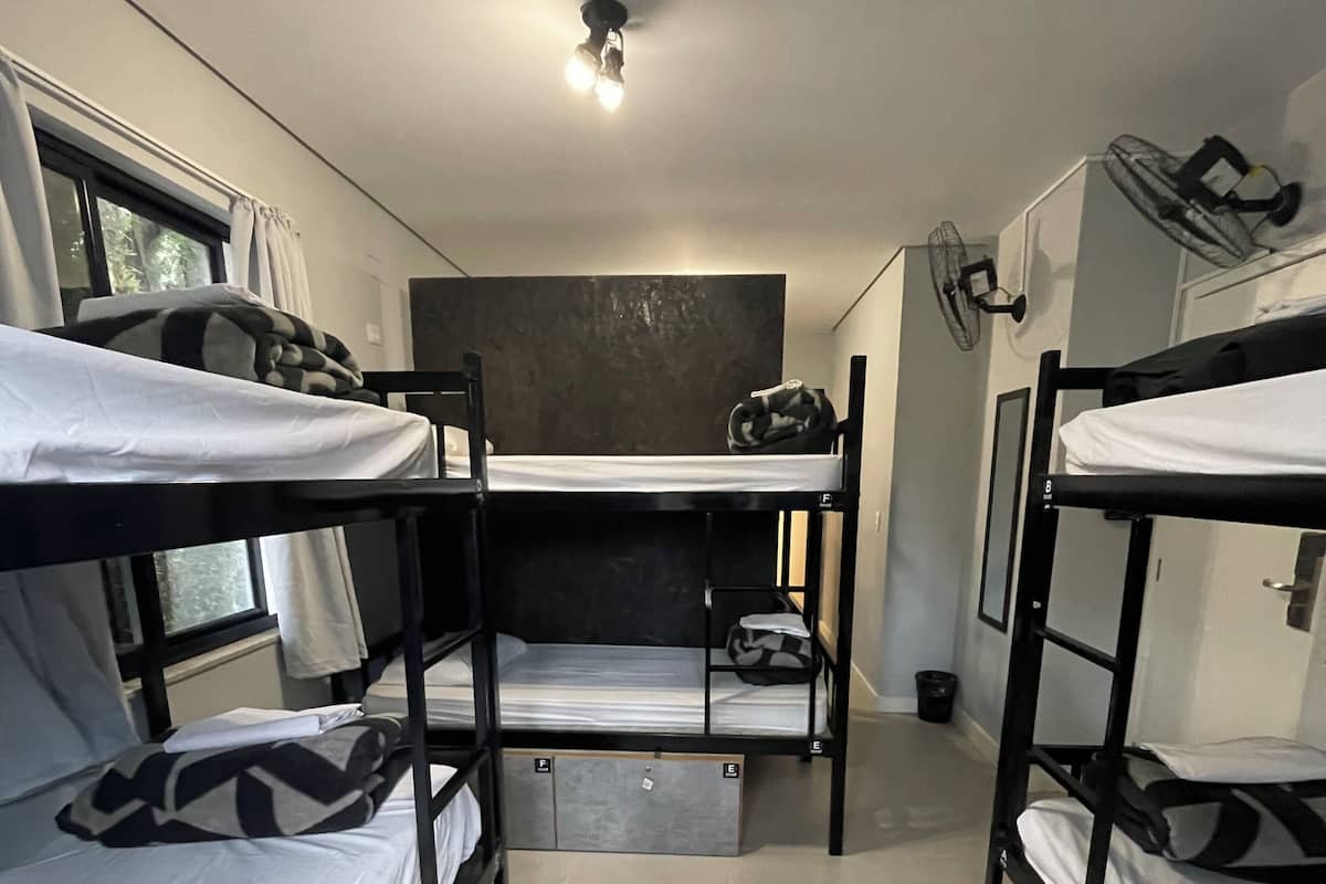 A dormitory room with bunk beds, a ceiling fan, and a window with curtains.
