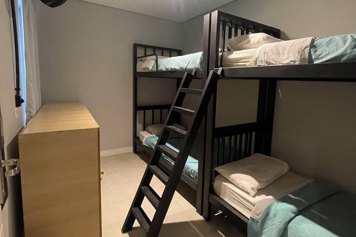A bunk bed room with a ladder, a small wooden desk, and a trash bin.