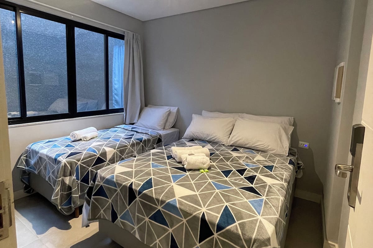 A hotel room with two beds, a large window, and a door.
