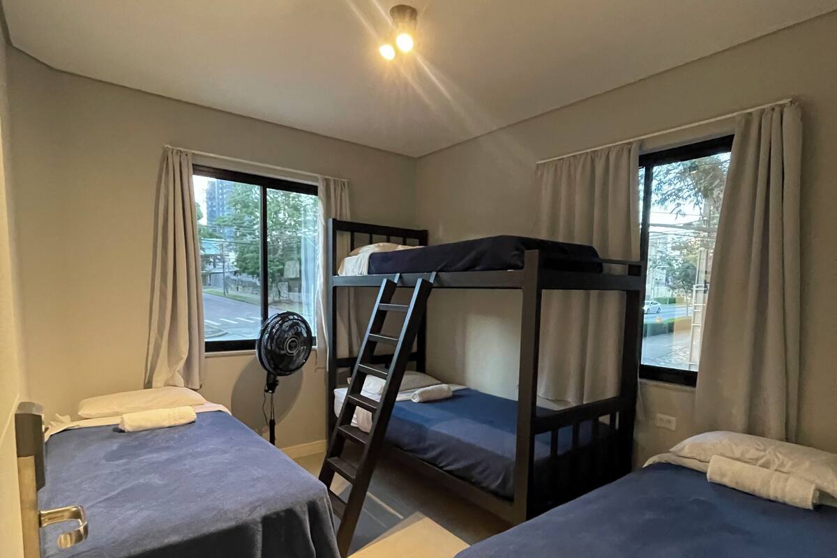A room with bunk beds, a fan, and a window with curtains.
