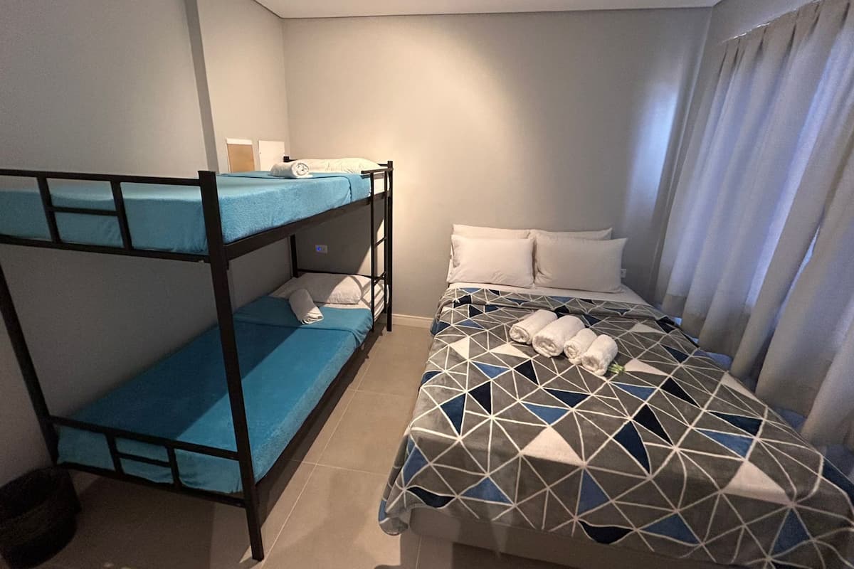 A room with bunk beds, a bed with a geometric patterned bedspread, and a window with curtains.
