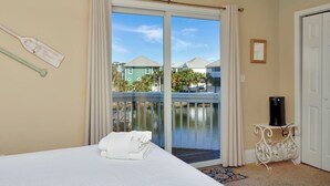 Camera d'albergo con un letto, un tavolino con una macchina per caffè, vista su un corpo d'acqua e un balcone con tende.