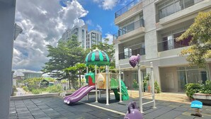 A playground with slides and climbing structures, surrounded by a paved area and residential buildings. - Apartment in District 7 Near SECC (Thành phố Hồ Chí Minh)