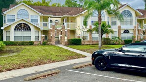 A two-story building with a central entrance, a covered porch, and a parking lot with a black car.