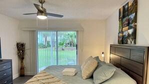 A bedroom with a bed, a ceiling fan, a nightstand, a dresser, and a view of the outdoors through a sliding glass door.
