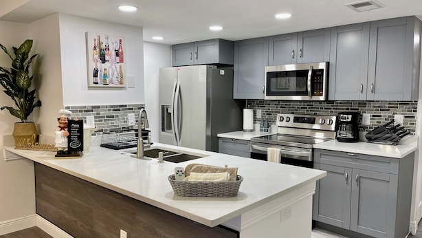 A modern kitchen with grey cabinets, stainless steel appliances, a central island, and a potted plant.