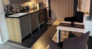 Moderni keittiö, jossa on sisäänrakennettu uuni, pesuallas sekä ruokailutila pöytineen ja tuoleineen.