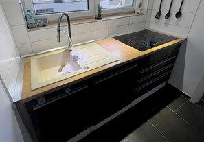 Een moderne keuken met een houten aanrecht, een roestvrijstalen spoelbak en een zwart fornuis, met een raam boven de spoelbak.