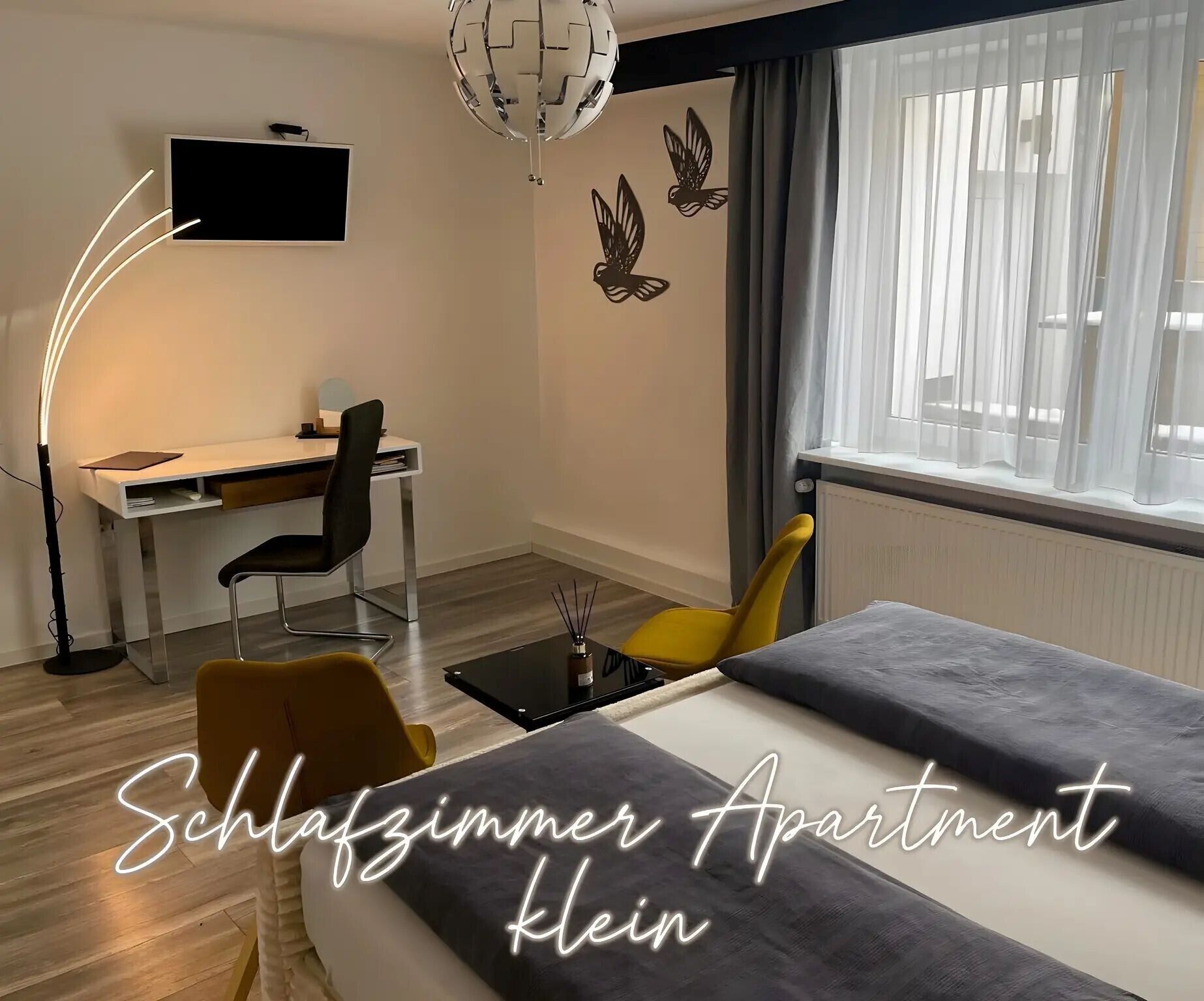 A bedroom with a bed, a desk, a chair, and a window with curtains.