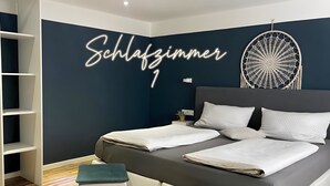 Ein modernes Schlafzimmer mit dunkelblauer Akzentwand, einem Bett mit weißer Bettwäsche, zwei Nachttischen und einem an der Wand befestigten Traumfänger.