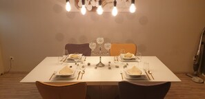 Mesa de comedor dispuesta con platos, cubiertos y vasos, con un centro de mesa decorativo e iluminación colgante.