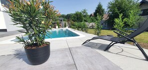 Una piscina con una silla de descanso, una planta en maceta y un área de patio.