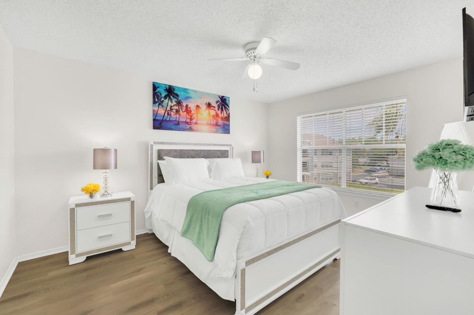 Une chambre moderne comprenant un lit, des tables de chevet, un bureau, un ventilateur de plafond et une fenêtre avec des stores.