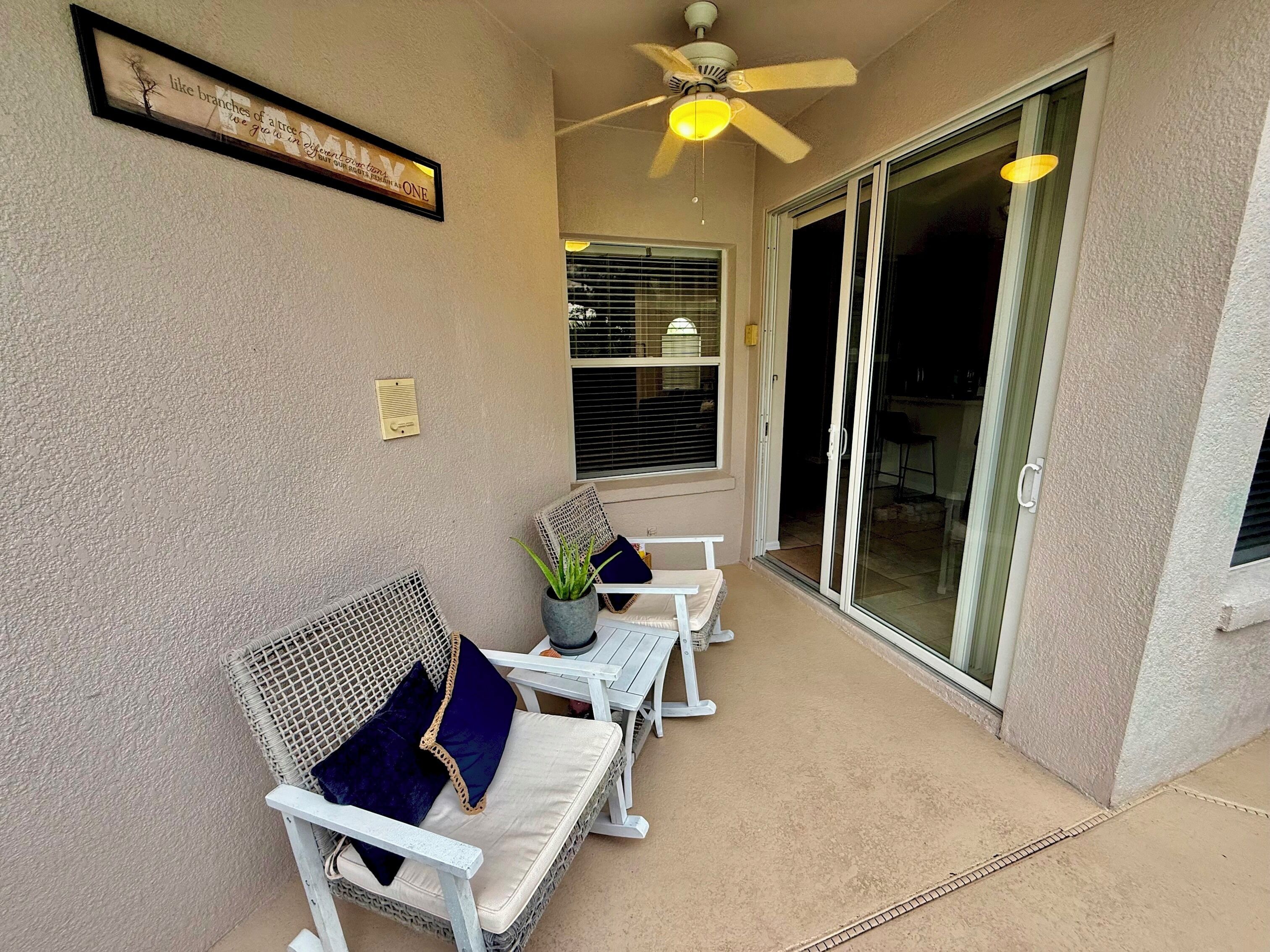 Ein überdachter Patio-Bereich mit Rattanmöbeln, einem Deckenventilator und einer Schiebetür zu einem Außenbereich.