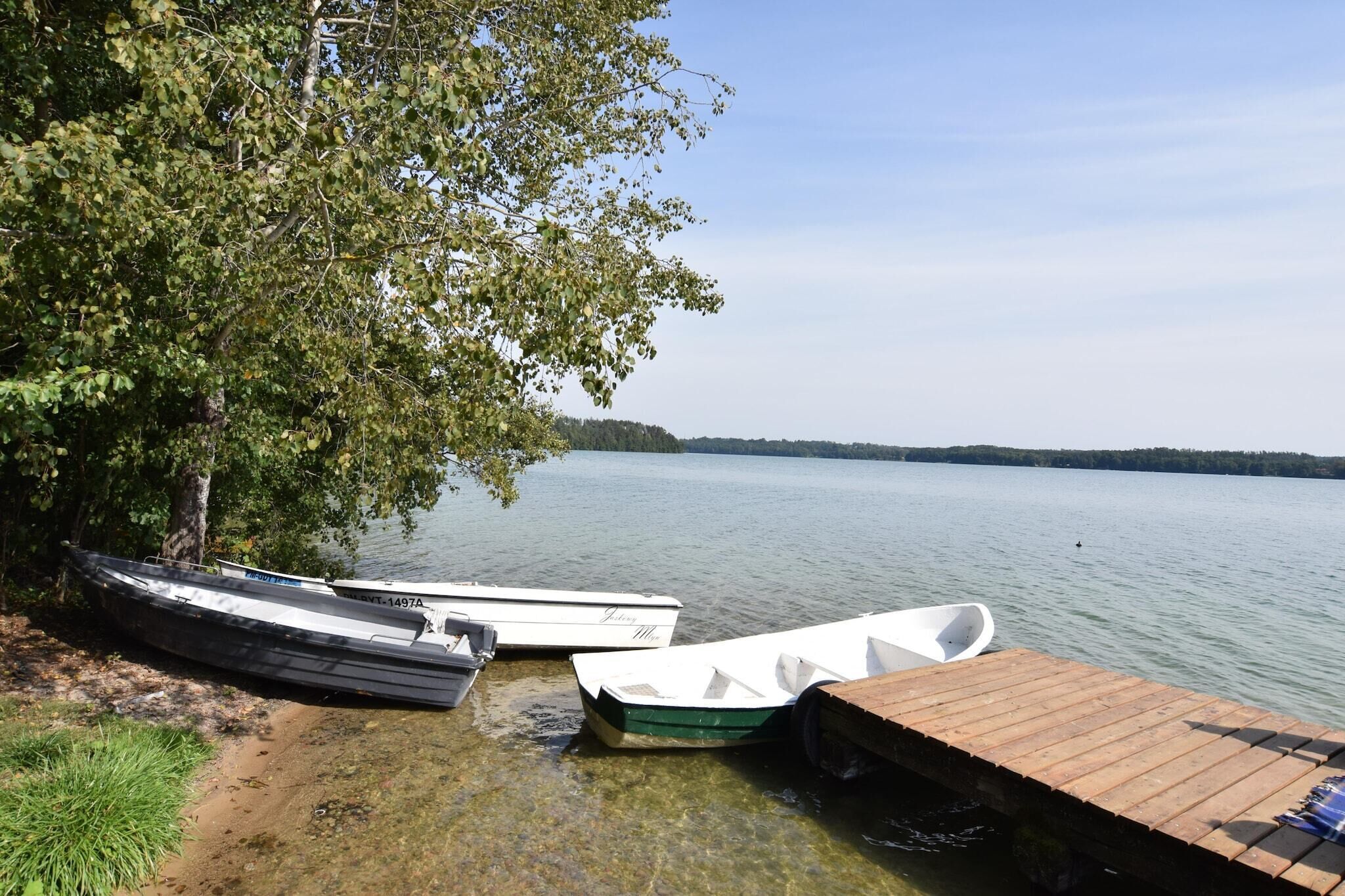 A dock with boats, a clear lake, and a forested shoreline.