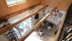 Een kamer met hoge houten plafonds en uitzicht op het omliggende landschap, voorzien van een geruit gordijn, een klein rond tafeltje met kopjes en een muur met ingelijste foto's.