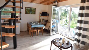 Een modern interieur met een houten trap, een eethoek met een tafel en stoelen, een keuken met een koelkast, en een grote schuifpui die leidt naar een terras.