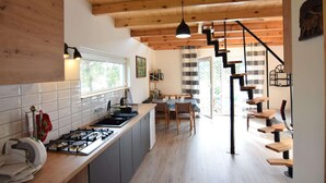 Een moderne keuken met een centraal eiland, houten balken in het plafond en een trap naar een eetgedeelte.