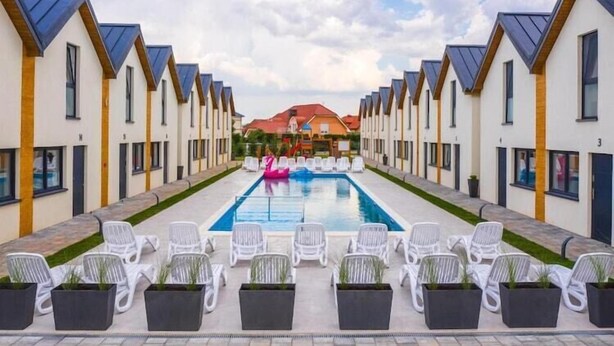 Filas de edificios modernos de una sola planta con una piscina central, rodeada de sillones blancos y plantas en macetas.