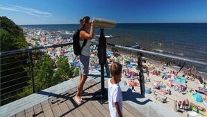 Un balcón con vista a una playa concurrida y al mar.
