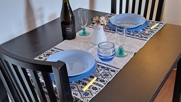 A dining table set with plates, glasses, and a bottle, surrounded by chairs. - Lovely and Charming Nest close to Porta Romana (Milano)