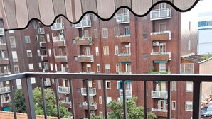 A balcony with a potted plant, a view of a red-tiled roof, and a building with balconies and windows. - Lovely and Charming Nest close to Porta Romana (Milano)