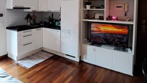 A compact kitchen with white cabinets, a black countertop, and a built-in TV displaying a sunset. - Lovely and Charming Nest close to Porta Romana (Milano)