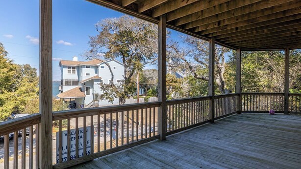 A covered wooden deck with a view of a house and trees. - Treetop Tides, Sound View and Canal Front 4BR 3BA Emerald Isle! (Emerald Isle)