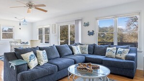 A spacious living room with a large sectional sofa, a glass coffee table, and a ceiling fan. - Treetop Tides, Sound View and Canal Front 4BR 3BA Emerald Isle! (Emerald Isle)