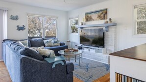 A living room with a large TV, a fireplace, and a sofa. - Treetop Tides, Sound View and Canal Front 4BR 3BA Emerald Isle! (Emerald Isle)