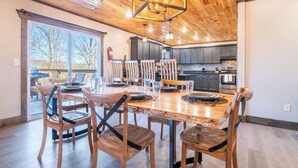 Een ruime eethoek met een houten tafel en stoelen, een moderne keuken op de achtergrond, en een groot raam met uitzicht op het landschap.