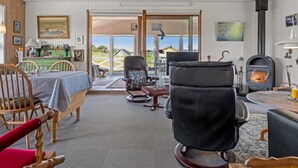 En hyggelig stue med pejs, et spiseområde med bord og stole, og udsigt udendørs gennem en glasdør.