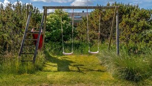 Et legesæt i træ i en græsmark med frodig buskads og træer i baggrunden.