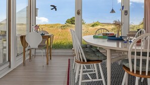 Et overdækket udendørs spiseområde med et bord og stole, med udsigt til et græsbevokset landskab.